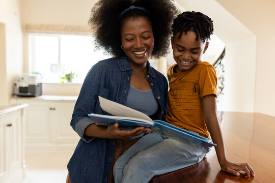 Mother and child reading book together in cozy kitchen, sharing joyful moment