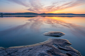 Skerries of Lake Ladoga, granite rock and small island, clouds flaming at dawn, reflected in calm...