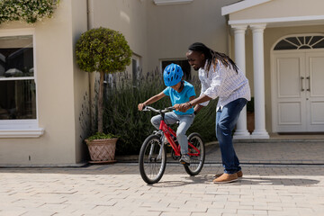 Fototapeta premium Father teaching son to ride bicycle in front of house, both smiling