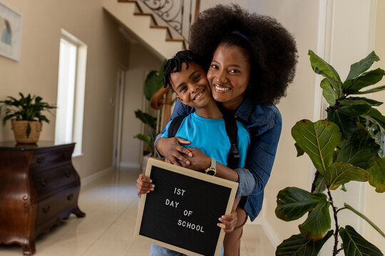 Mother and son smiling, holding sign for first day of school at home - Powered by Adobe