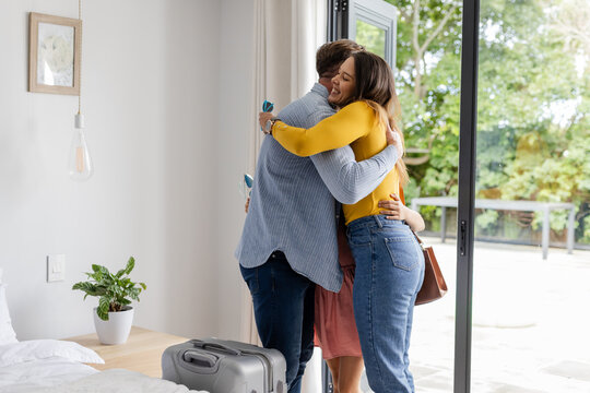 Family embracing warmly by open patio door, suitcase on floor, enjoying reunion