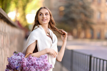 Fototapeta premium Smiling woman with basket of lilac flowers on city street