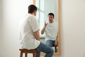 Handsome man looking at himself in mirror indoors