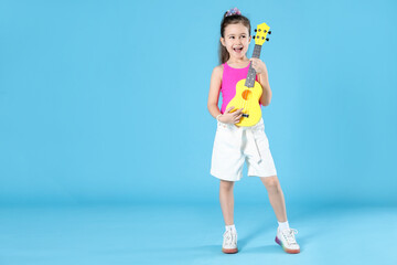 Fototapeta premium Cute girl playing toy guitar on light blue background