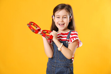 Cute girl playing toy tambourines on yellow background