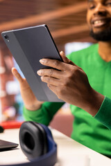 Man at home taking break from work to look at social media feed on tablet. Remote employee at work in apartment office pausing tasks to use social network application on device, close up