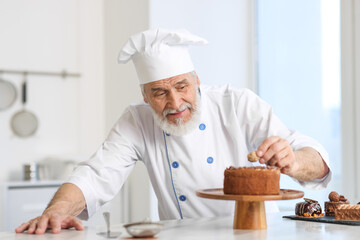 Elderly pastry chef decorating tasty cake at table in kitchen