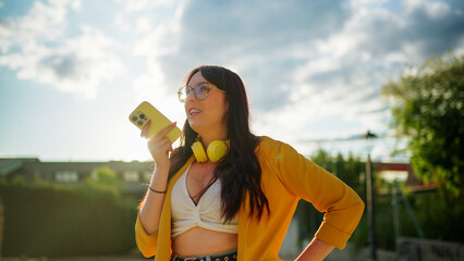 Smiling young woman recording a voice message on her phone outside