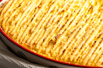 Potato casserole in a porcelain, red baking dish with a white towel on a gray background. Close-up.