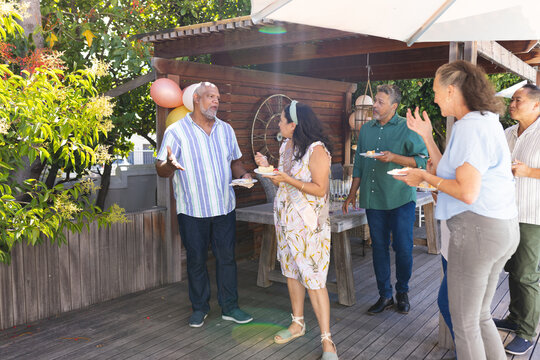 Seniors enjoying outdoor birthday party, sharing laughter and cake on wooden deck - Powered by Adobe