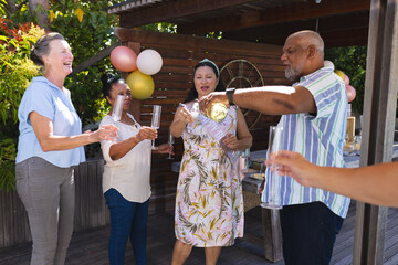 Celebrating outdoors, seniors pouring champagne and laughing with friends in garden