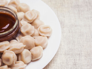 Russian dumplings on a white plate with brown sauce in a glass small jar and fresh cut tomatoes. Popular East European meal. Simple tasty food.