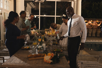 African American man celebrating with friends at elegant dinner party by poolside