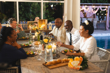 Seniors enjoying dinner party, sharing laughter and wine by poolside at night
