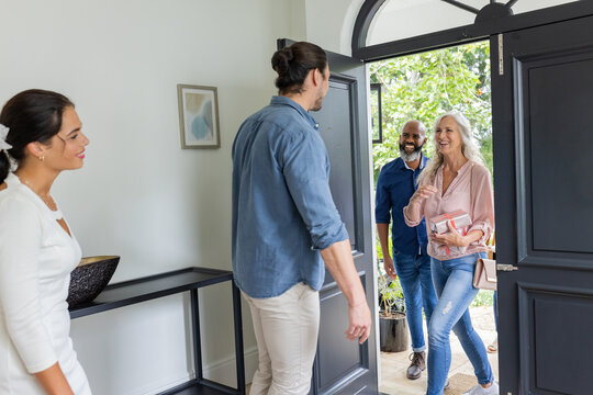 Welcoming guests at home, smiling couple greeting friends at front door