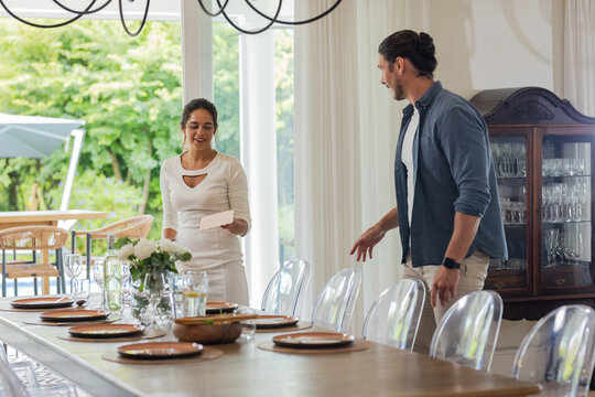 Preparing elegant dining table for wedding, couple smiling and arranging plates