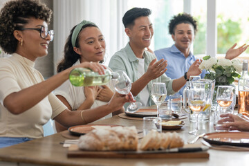 Pouring wine, friends laughing around dinner table with bread and flowers