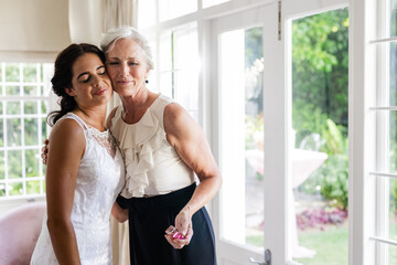 Embracing older woman, bride smiling warmly in sunlit room, celebrating together