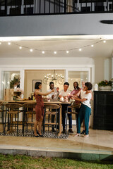 Friends celebrating with champagne outdoors, toasting under string lights at night © wavebreak3