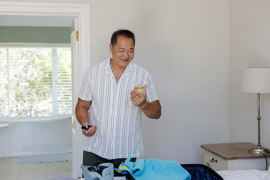 Packing suitcase at home, man holding smartphone during travel preparations