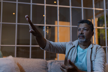 Senior man gesturing enthusiastically while sitting on sofa at home in evening
