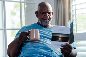 Senior man enjoying quiet time reading book and drinking coffee at home