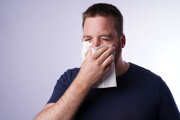 Naklejka premium Young guy with ginger beard blows his nose in a tissue.