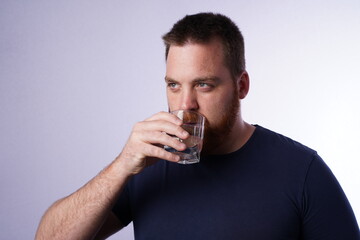 Young male adult with blue eyes and ginger beard drinking water from a glass cup. 