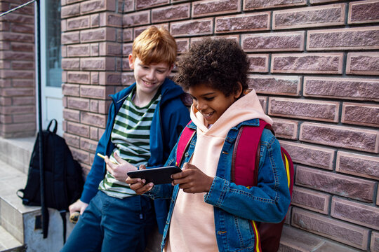 Young boys playing video games on their smart phone after skipping school and sitting on a sidewalk in the city - Powered by Adobe