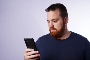 Young guy with ginger beard and blue eyes looking at his mobile phone. Young male adult with ginger...