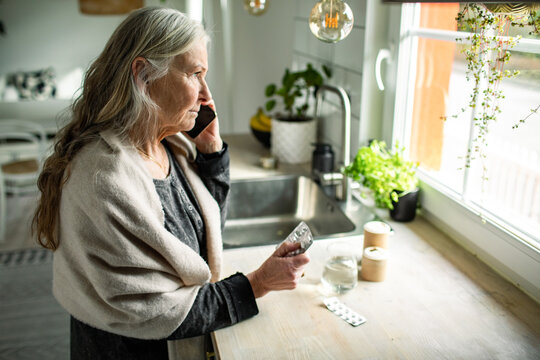 Senior caucasian woman talking to her doctor on her phone while taking pills and perscription drugs at home
