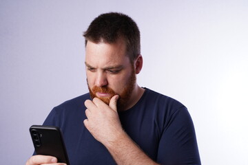 Young guy with ginger beard and blue eyes looking at his mobile phone. Young male adult with ginger...