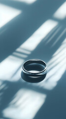 Silver wedding band on reflective surface, window light patterns background; perfect for wedding announcements or jewelry websites