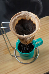 Café sendo coado em filtro de pano sobre xícara verde esmaltada.