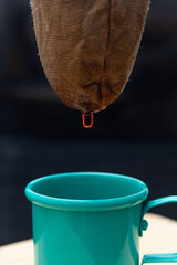 Detalhe de gota de café pingando do coador para uma xícara verde.
