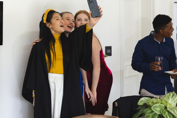 Teens celebrating graduation taking selfie at home, smiling and enjoying party