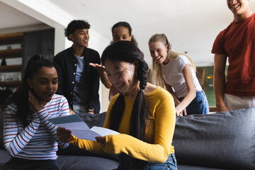 Teen girl reading letter on couch, friends celebrating exciting news together