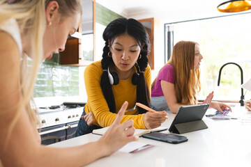 Teen girls collaborating on school project at home, using tablet and notes