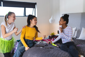 Teen girls laughing and chatting while planning outfits on bed at home