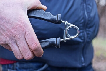 one hand squeezes black gray sports expander against blue clothes on spring city street