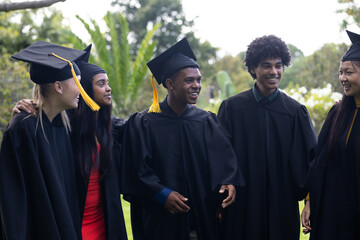 Graduating students in caps and gowns celebrating together outdoors, smiling happily