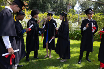 Graduating students in caps and gowns holding diplomas and celebrating outdoors