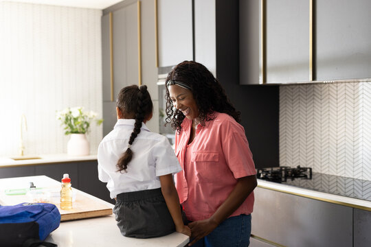 Preparing daughter for school, African American mother smiling in modern kitchen
