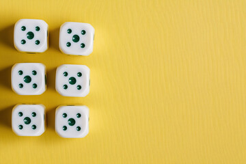 Six white dice showing the number five arranged neatly on a vibrant yellow background space.