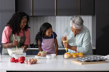 Three generations baking cupcakes together in modern kitchen, sharing joyful moments