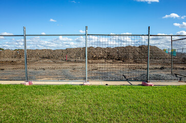 Fototapeta premium Construction site behind temporary fencing with dirt piles and leveled ground in suburban Australia—concept of land development, infrastructure preparation, and urban expansion.