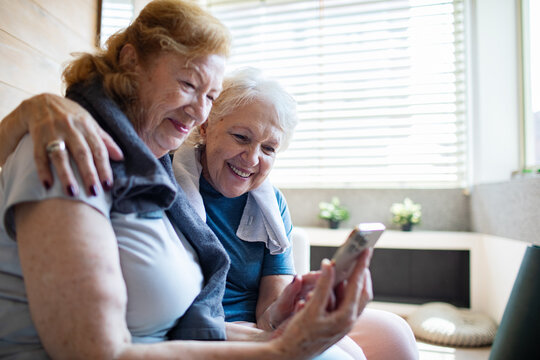Senior lesbian couple laughing while looking at smartphone after home workout