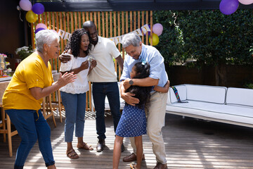 Celebrating birthday outdoors, grandfather hugging granddaughter, family smiling and clapping