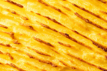 A background with the texture of mashed potatoes baked until golden brown in the oven. Close-up, macro photography. Use for menu and banner.