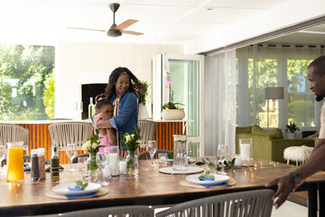 African American mother hugging daughter while father sets dining table at home